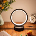 Glow & Drift Eclipse Minimalist Halo Lamp casting a warm white ambient glow on a wooden desk with a flower vase and a clock