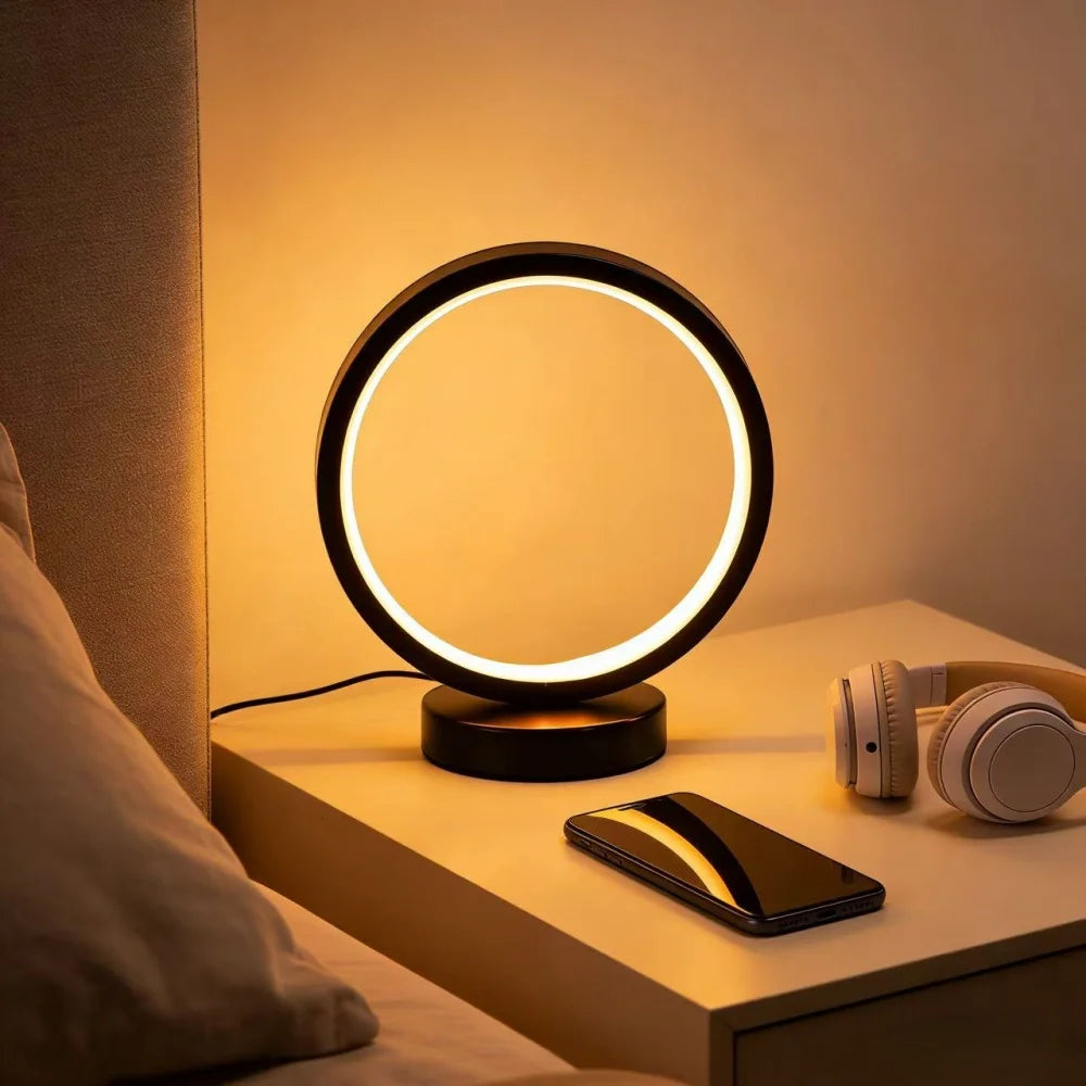 Glow & Drift Eclipse Minimalist Halo Lamp on a nightstand casting warm halo ambient lighting next to headphones and a smartphone