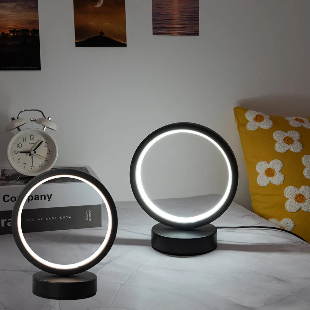 Glow & Drift Eclipse Minimalist Halo Lamp shown in two sizes next to a white alarm clock and a yellow floral pillow