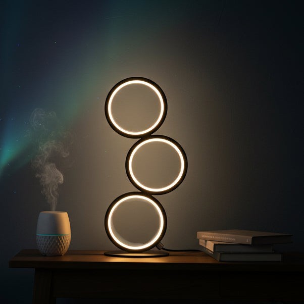 Glow & Drift Eclipse Triple Ring Table Lamp with modern sculptural black circles emitting soft ambient light on a desk.