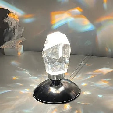 A close-up view of the Aether Crystal Projector, highlighting its faceted crystal shade, integrated power cable, and sleek metallic base while emitting a bright refracting light.