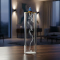 Premium clear glass cylindrical incense tower displaying hypnotic descending smoke trails from a top-mounted incense cone, set in a moody modern apartment interior at dusk.