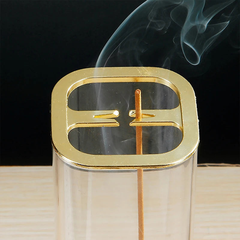 Detailed macro shot of the minimalist gold metal top clip holding an upside-down incense stick, with wisps of fragrant smoke rising against a dark studio background.
