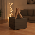 The Bonfire Flame Aroma Diffuser in a sleek black finish, placed on a wooden table against a warm, comforting backdrop of glowing string lights.