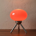 Glow & Drift Alva Bauhaus table lamp with a glowing orange mushroom glass shade and polished chrome tripod base.