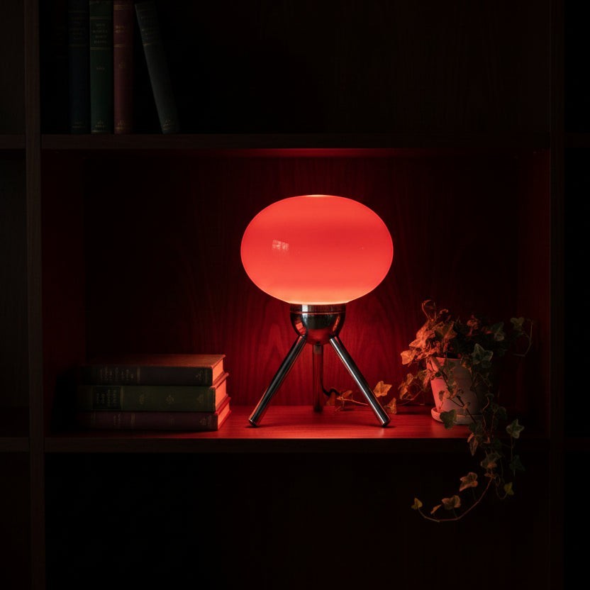 Glow & Drift Alva Bauhaus table lamp with a glowing red mushroom glass shade and polished chrome tripod base on shelf