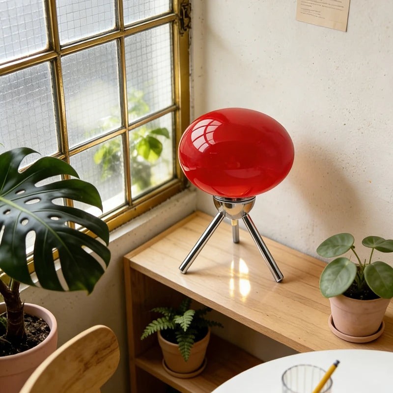 Glow & Drift Alva Bauhaus table lamp with a vibrant red glass mushroom shade and polished chrome tripod base on a shelf.