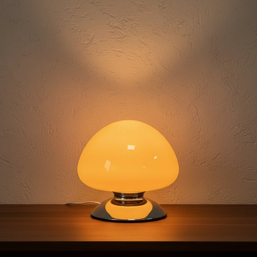 Glow & Drift Aura glass mushroom table lamp with a warm glowing dome and polished chrome base on a wooden surface.