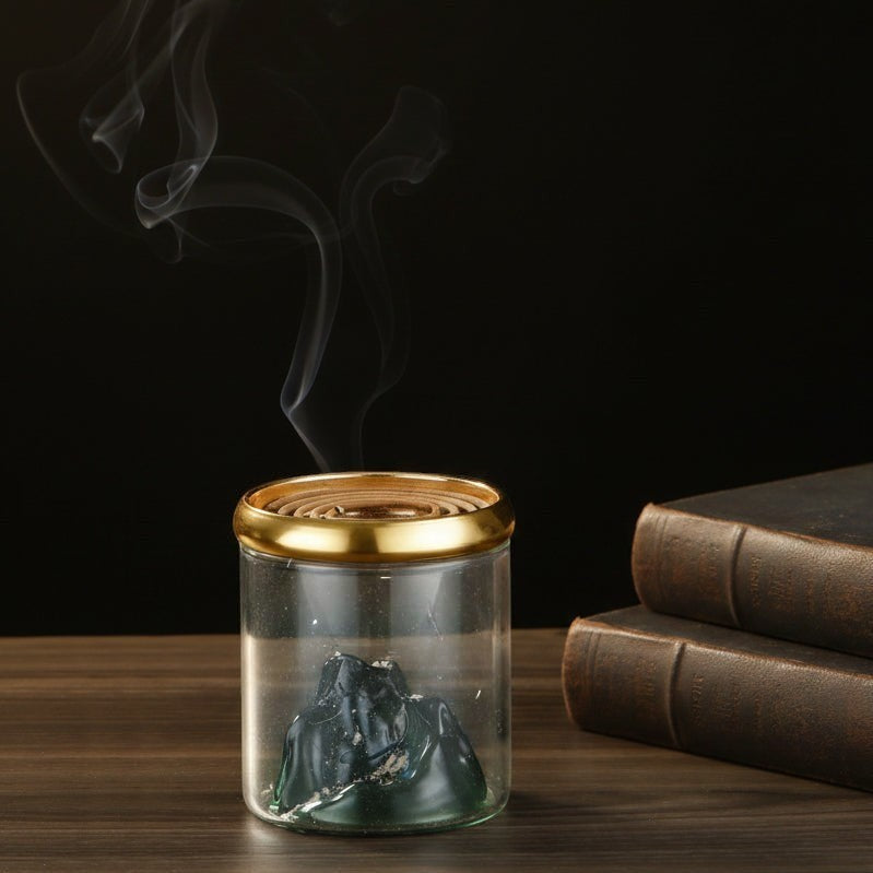 Glow & Drift Azure Peak backflow incense burner with blue glass mountain, gold lid, and cascading smoke on a table.