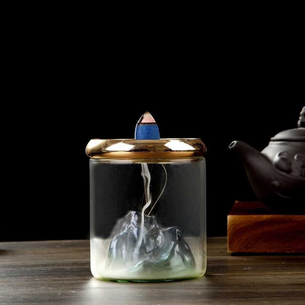 Glow & Drift Azure Peak backflow incense burner with a blue glass mountain inside a clear cylinder and gold mesh lid.