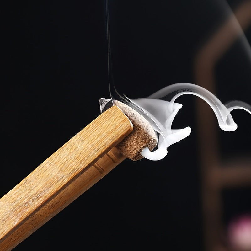 Glow & Drift backflow incense cone held by wooden tongs releasing a mesmerizing downward stream of white smoke