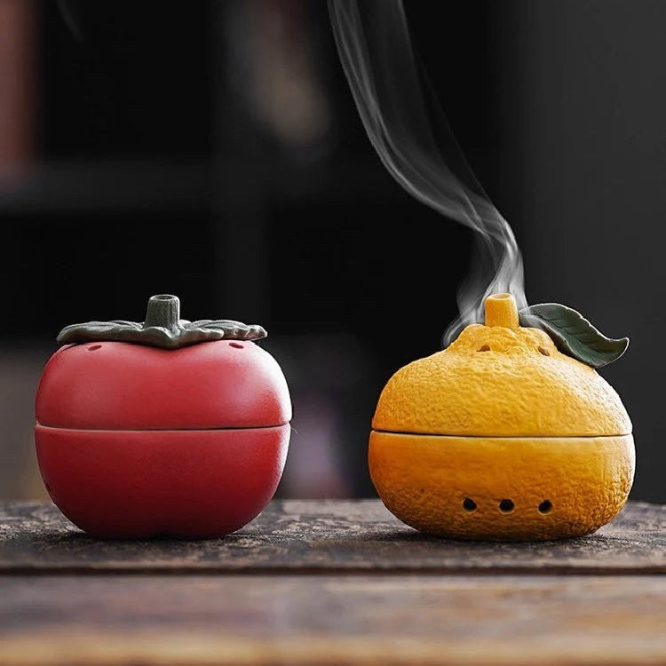 Glow & Drift ceramic incense vessels shaped like a red persimmon and a textured orange tangerine with smoke rising.