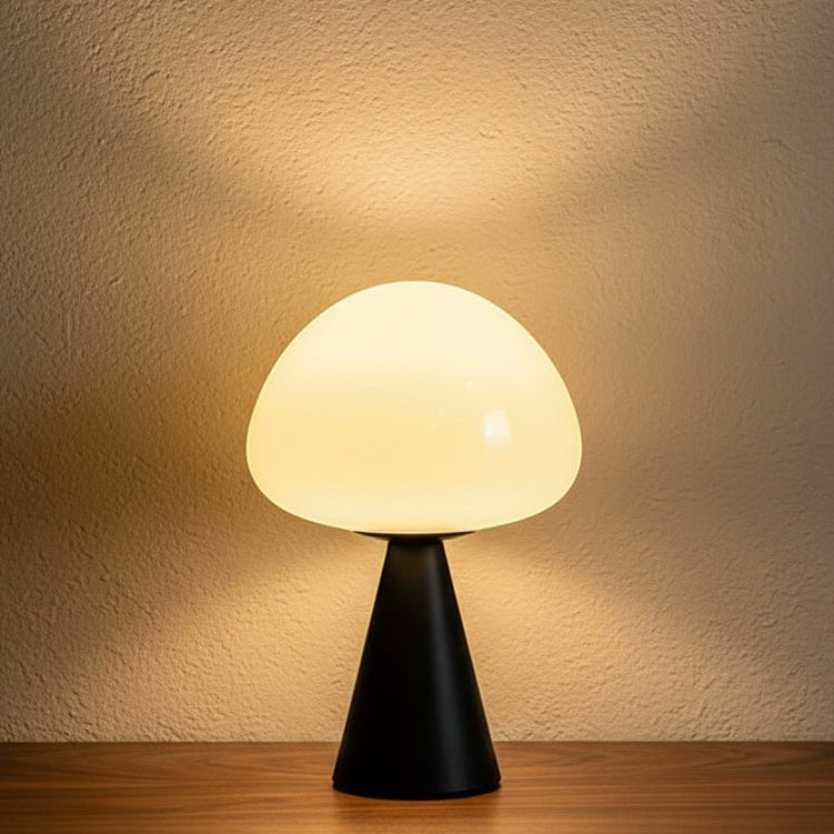Glow & Drift Eclipse mushroom table lamp with a matte black iron base and glowing white glass dome on a wooden table.