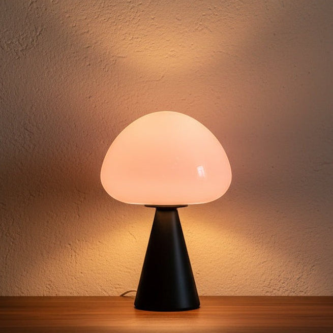 Glow & Drift Eclipse mushroom table lamp with a matte black iron base and glowing white glass dome on a wooden surface.