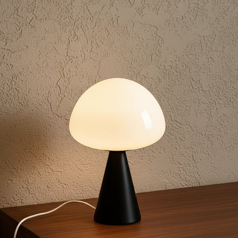 Glow & Drift Eclipse mushroom table lamp with a matte black iron base and glowing white glass dome on a wooden surface.