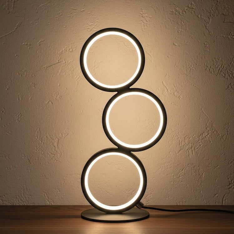 Glow & Drift Eclipse Triple Ring Table Lamp with a modern sculptural design emitting warm ambient light on a desk.