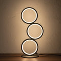 Glow & Drift Eclipse Triple Ring Table Lamp with a modern sculptural design emitting warm ambient light on a desk.