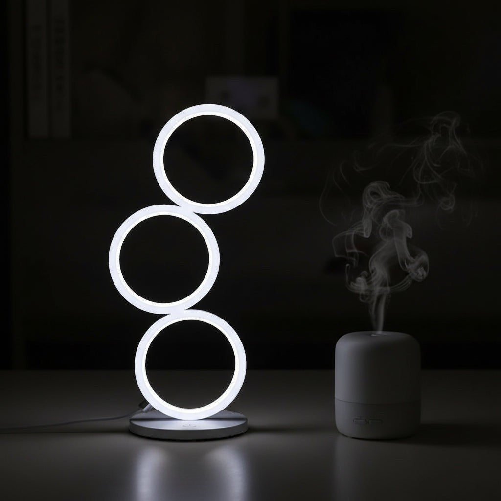 Glow & Drift Eclipse Triple Ring Table Lamp with modern sculptural design emitting soft white light on a dark desk