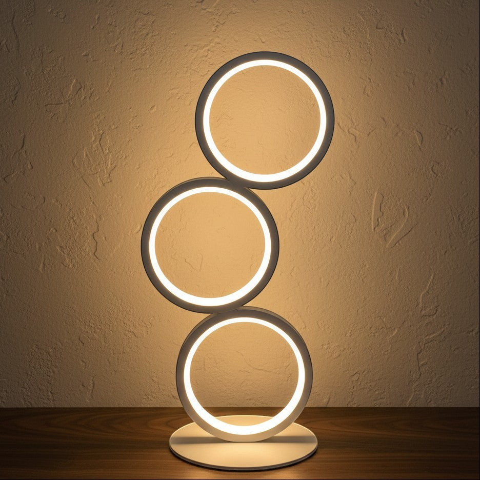 Glow & Drift Eclipse Triple Ring Table Lamp with a modern sculptural design emitting warm ambient light on a desk