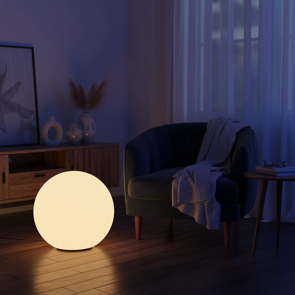 Glow & Drift Ethereal Orb Lamp glowing on a dark wooden floor in a cozy living room with a velvet armchair.