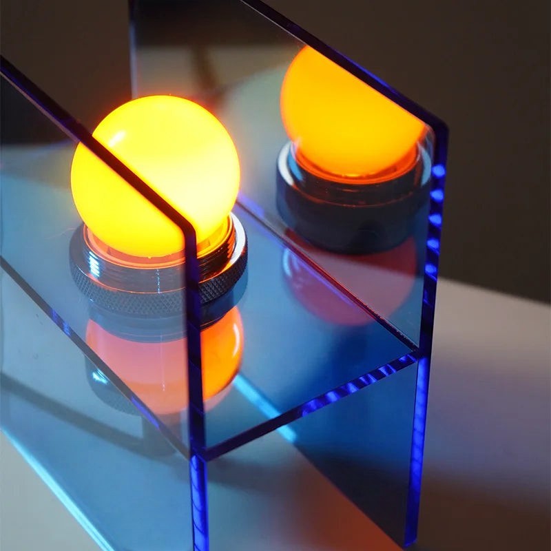 Glow & Drift Horizon geometric table lamp with blue acrylic panels and a warm glowing E27 bulb on a desk.