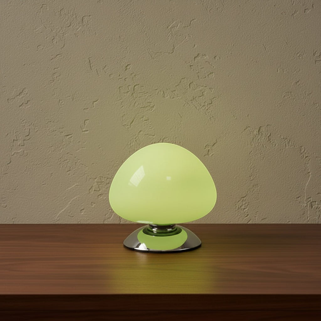 Glow & Drift Aura glass mushroom table lamp with a glowing light green dome and polished chrome base on a wood table.