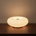 Glow & Drift Halo Donut Spectrum portable lamp on a dark wooden surface against a wall.