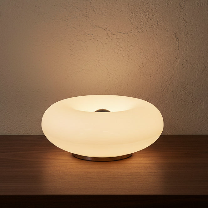 Glow & Drift Halo Donut Spectrum portable lamp on a dark wooden surface against a wall.