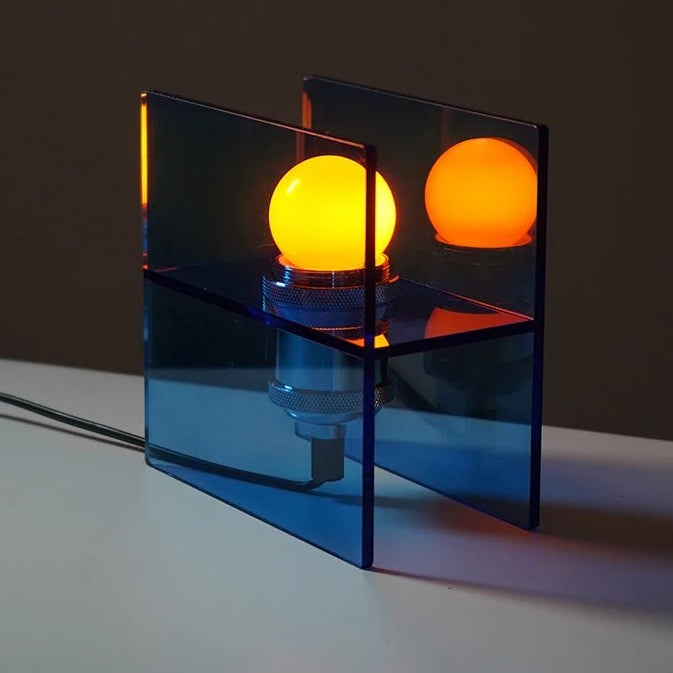 Glow & Drift Horizon geometric table lamp with blue acrylic panels and a warm glowing bulb on a white surface.