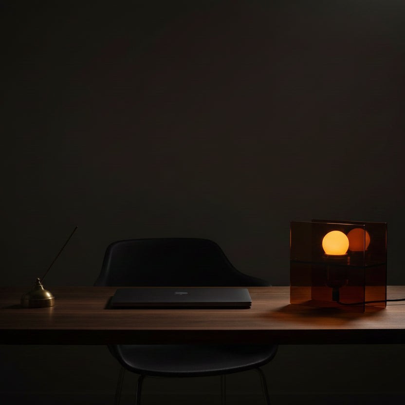 Glow & Drift Horizon geometric table lamp with amber acrylic panels casting a warm glow on a dark wooden desk.