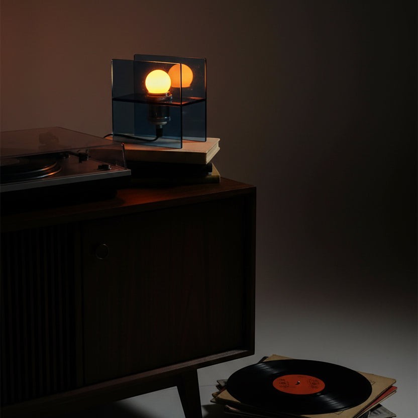 Glow & Drift Horizon geometric table lamp with blue tinted acrylic panels casting a warm glow on a wooden cabinet.