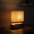 Glow & Drift Koto Japandi table lamp with a solid wood base and warm glowing organic linen shade on a dark surface
