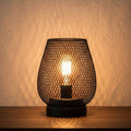 Glow & Drift Lumina Cage Retro Filament Lamp with a black iron mesh frame and warm glowing Edison bulb on a table.