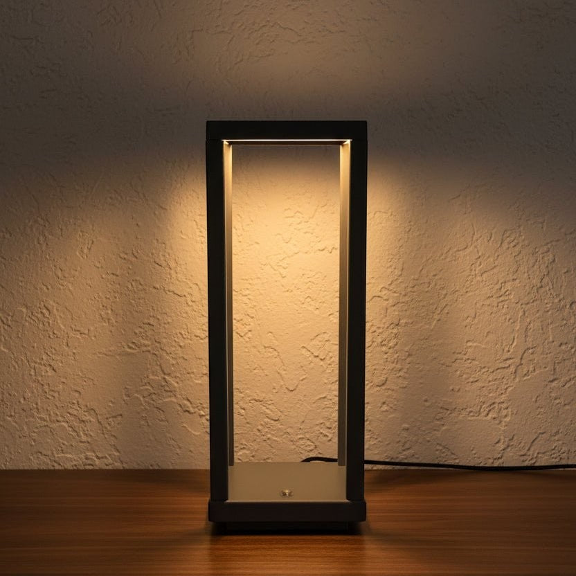 Glow & Drift Nomad Lantern, a minimalist black geometric cordless lamp casting a warm, soft glow on a wooden surface.