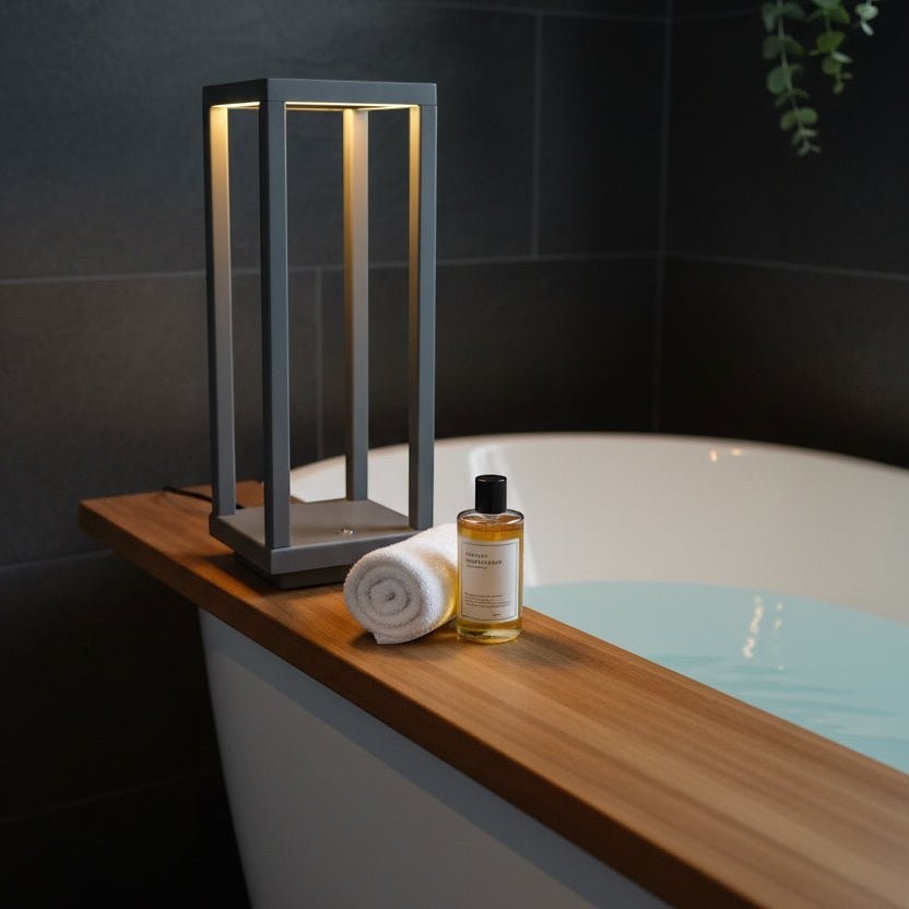 Glow & Drift Nomad Lantern, a grey cordless geometric lamp providing warm ambient light on a wooden bathtub tray.