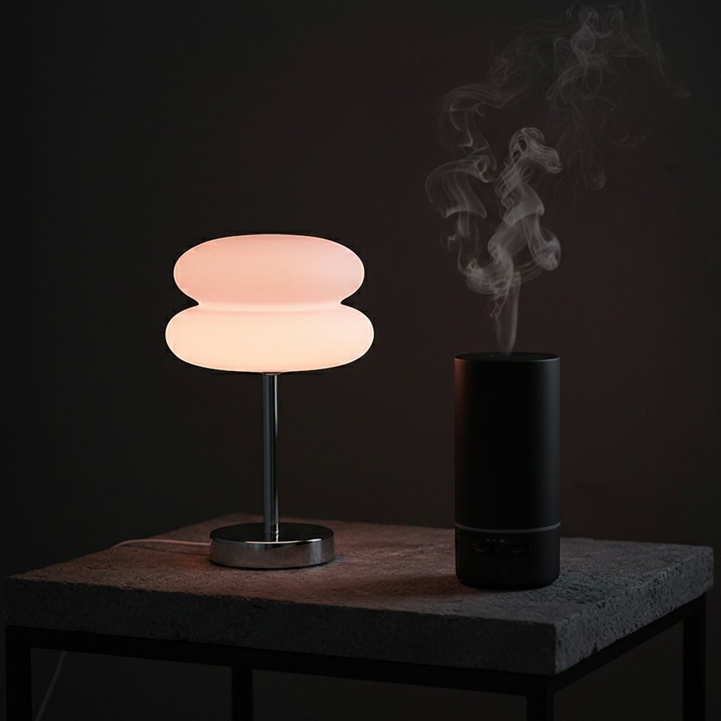 Glow & Drift Retro Macaron glass lamp with a polished steel base emitting a soft warm glow next to a black diffuser.