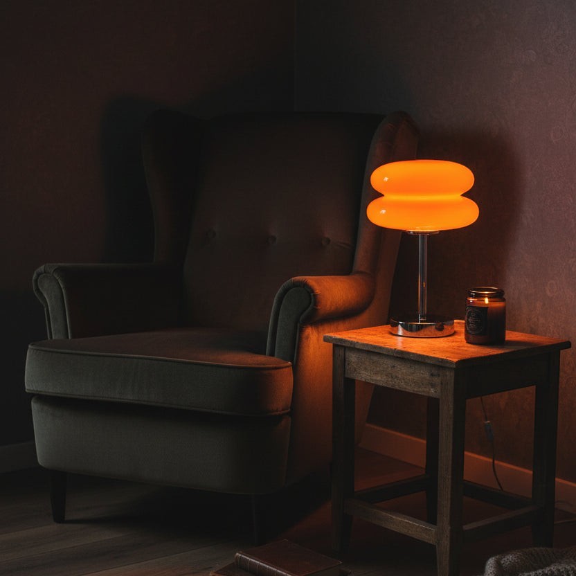 Glow & Drift Retro Macaron glass lamp with orange shade and polished steel base on a wooden side table by an armchair.