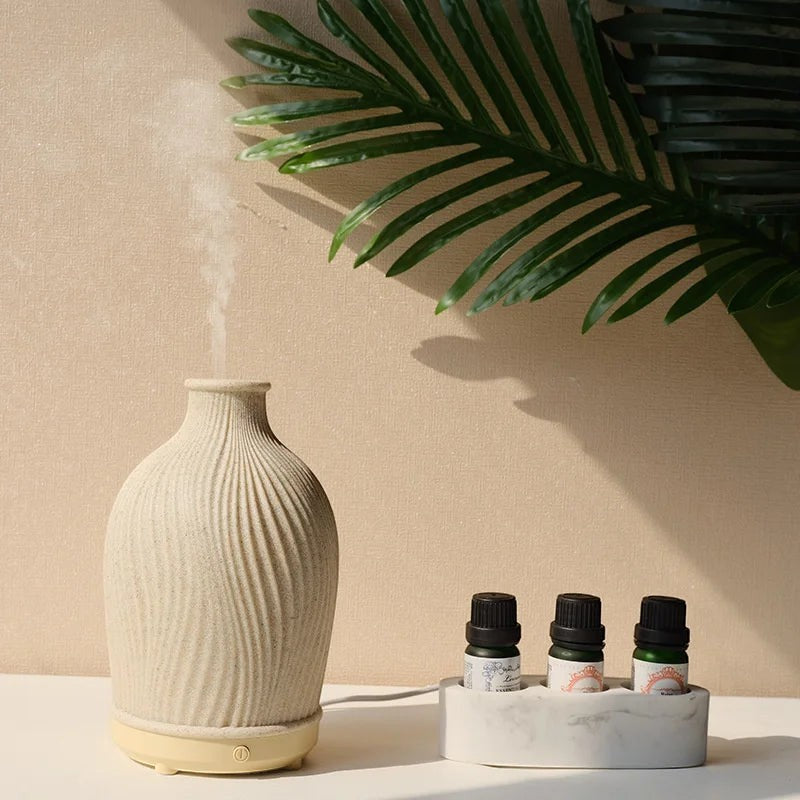 Glow & Drift Earthen Vase aroma diffuser with ribbed resin texture emitting mist next to essential oil bottles