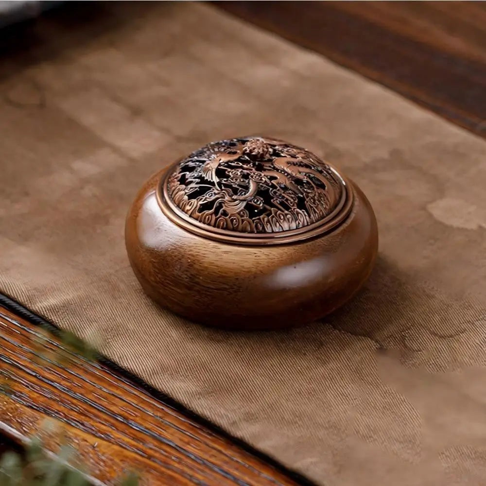 Glow & Drift solid wood incense burner with an intricate antique-style metallic lid on a brown fabric table runner.