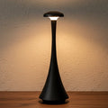 Glow & Drift Spora portable mushroom lamp in matte black with a soft, warm ambient glow on a wooden surface.