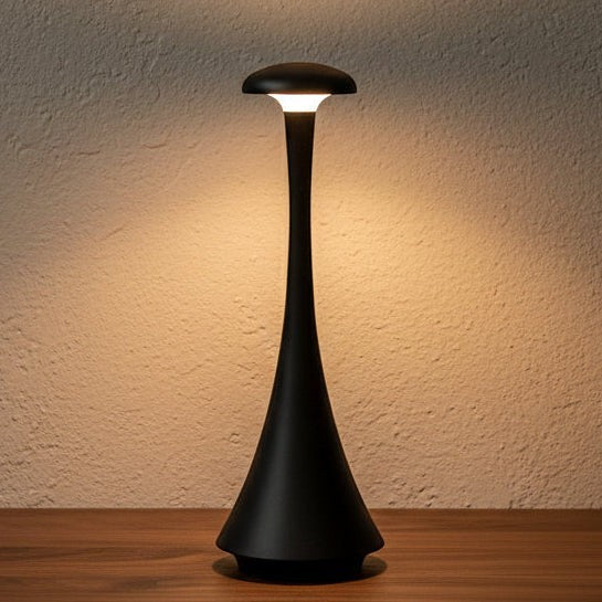 Glow & Drift Spora portable mushroom lamp in matte black with a soft, warm ambient glow on a wooden surface.