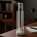 Glow & Drift Zenith suspended glass incense burner with a white iron frame and smoke rising from an incense stick