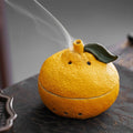 Glow & Drift textured tangerine ceramic incense burner with smoke drifting from the stem on a dark surface.
