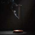 Glow & Drift Equinox walnut incense stand with a vertical metal arm suspending a burning incense stick over a wood base