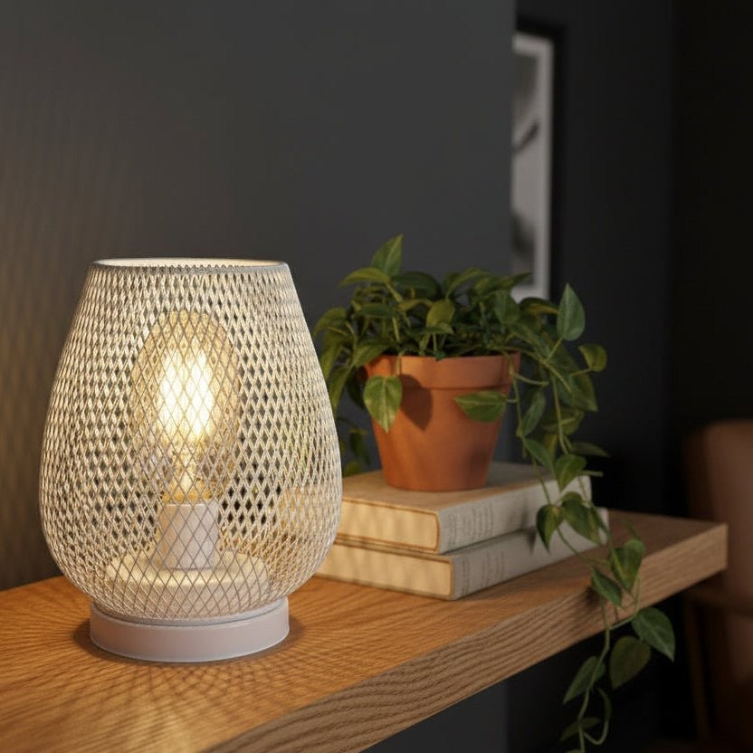 Glow & Drift Lumina cage lamp with white iron mesh frame and warm Edison filament bulb on a wooden shelf.