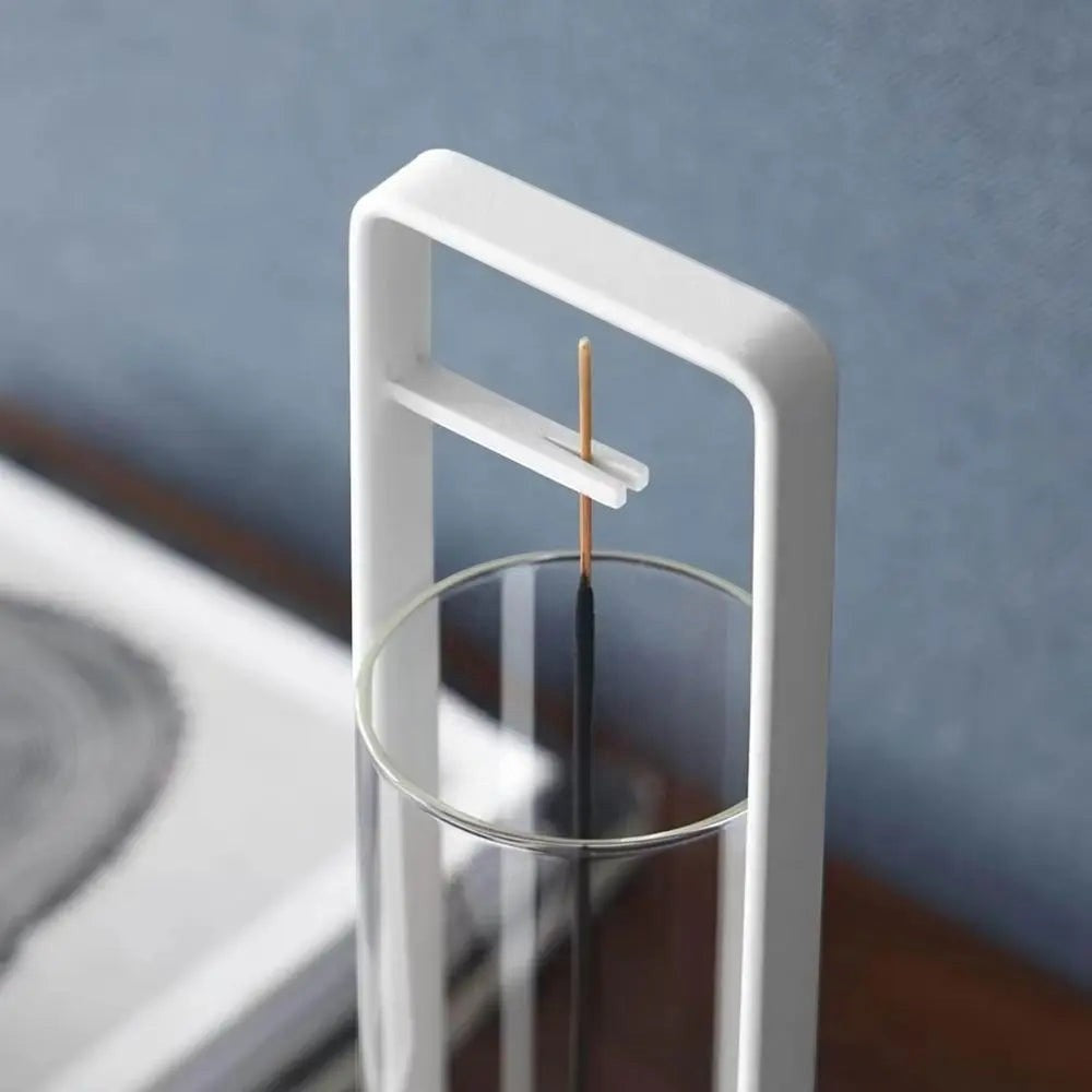 Glow & Drift Zenith suspended incense burner featuring a white iron frame and clear glass ash-catching cylinder.