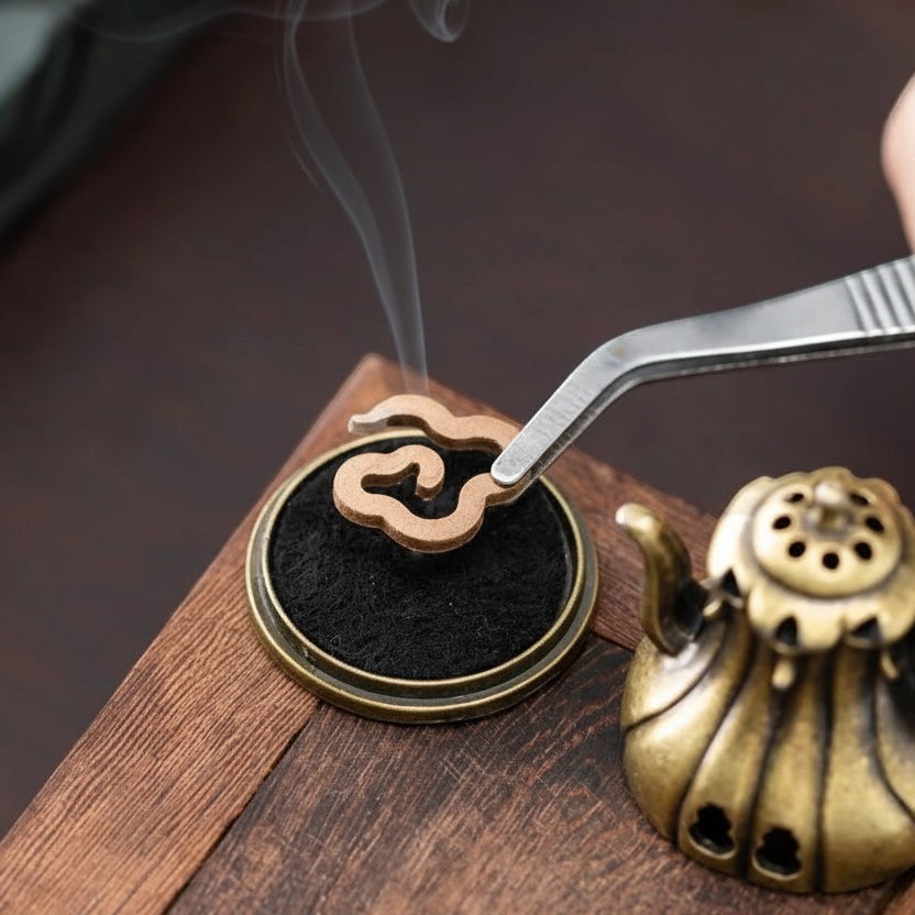 Glow & Drift Xiangyun cloud-shaped natural incense being placed with tweezers on a brass burner in a cozy setting