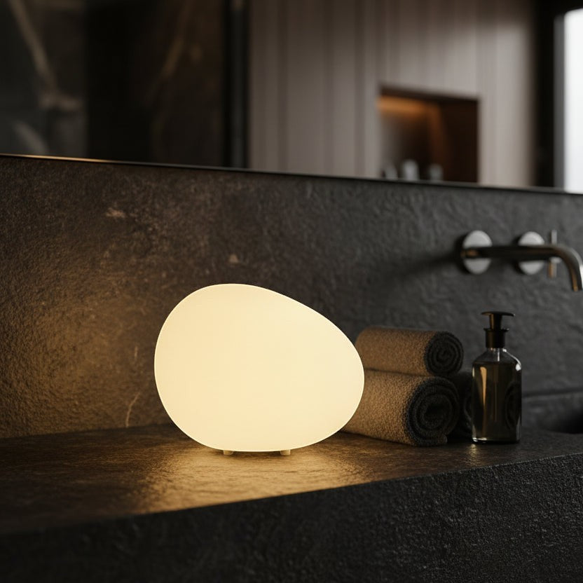Glow & Drift Zen Riverstone Ambient Lamp with a smooth frosted acrylic cobblestone design glowing on a dark bathroom counter