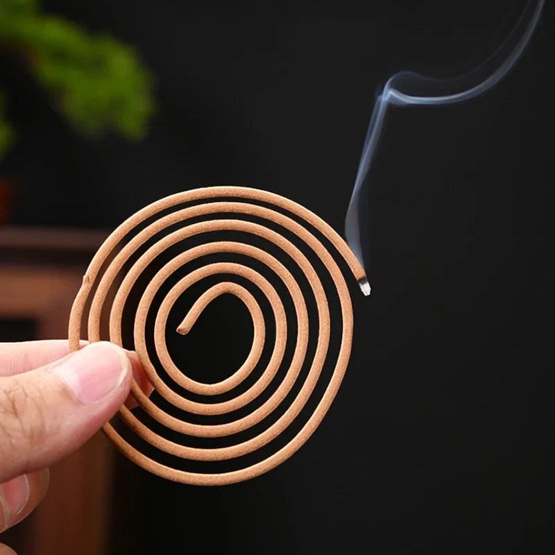 Glow & Drift Zenith Ritual Coil Incense burning with thin fragrant smoke in a hand against a dark background