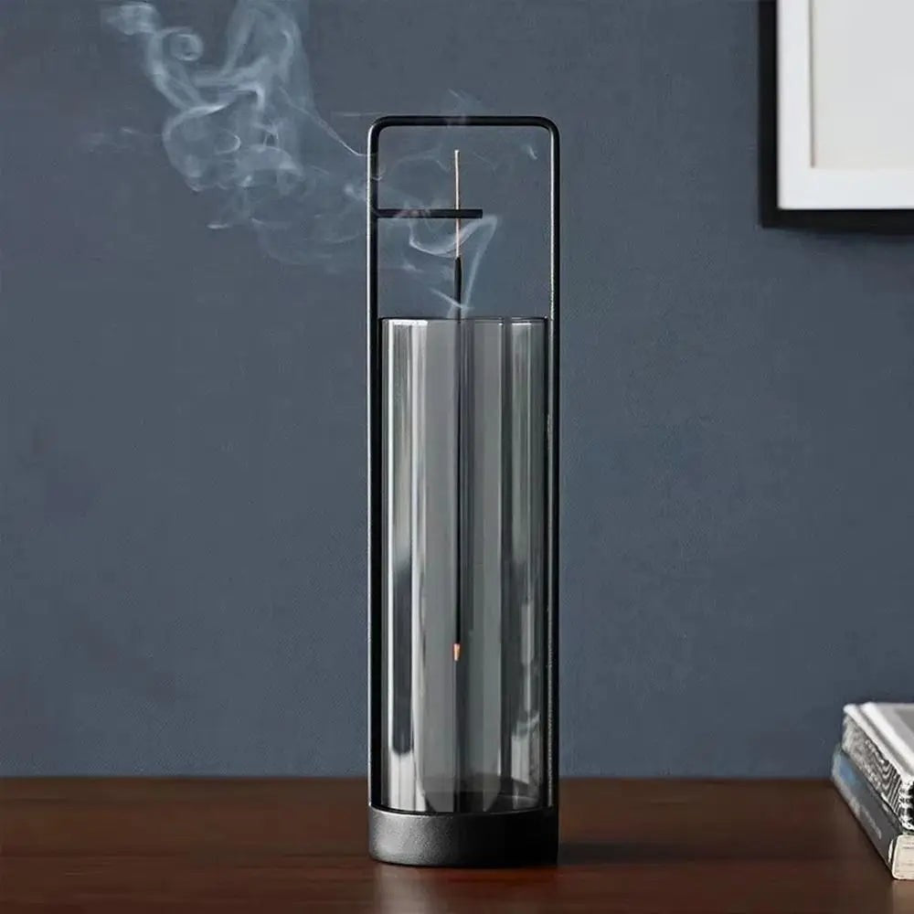 Glow & Drift Zenith suspended glass incense burner with a black iron frame and smoke rising inside the cylinder.